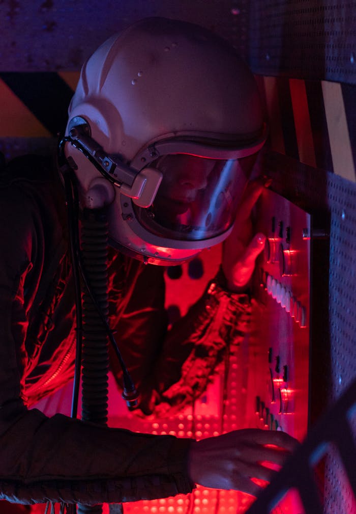 A female astronaut in a spacesuit operates a control panel with a red glow.